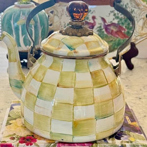 May include: A tea kettle featuring a hand-painted checkered pattern in shades of cream, sage green, and yellow. The kettle has a metal handle with a wooden grip, a brass-toned lid finial, and a matching lid with a decorative metal base.