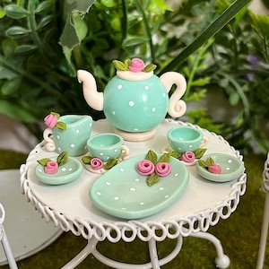 Könnte beinhalten: Ein Miniatur-Tee-Set mit Teekanne, Milchkännchen, Zuckerdose und zwei Tassen mit Untertassen. Das Set ist in hellblau mit weißen Punkten und rosa Blumen bemalt.