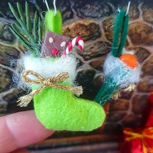 Könnte beinhalten: Zwei grüne Filz-Weihnachtsstrümpfe mit weißem Pelzbesatz. Ein Strumpf ist mit einem Zuckerstangen, einem Stück Schokolade und einem Zweig grüner Kiefer gefüllt. Der andere Strumpf ist mit einer kleinen orangefarbenen Kugel gefüllt.