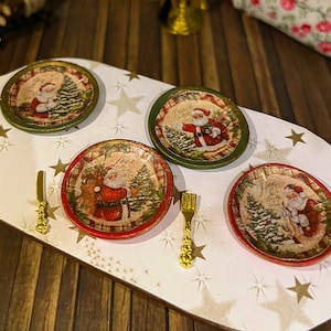 Könnte beinhalten: Vier Miniatur-Weihnachtsteller mit einem Weihnachtsmann-Motiv. Jeder Teller zeigt ein anderes Weihnachtsmann-Design in Grün- und Rottönen. Die Teller befinden sich auf einer weißen Oberfläche mit goldenen Sternen.