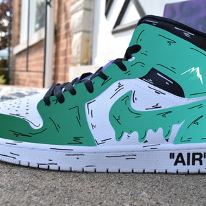 May include: White and green high-top sneakers with black accents and a black and white 'AIR' logo on the side. The sneakers have a green and white paint design with black outlines.