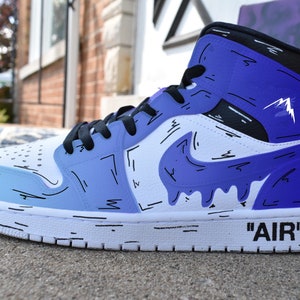 May include: White high-top sneakers with a blue and white gradient design. The sneakers have black accents and a black swoosh logo with a dripping effect. The text 'AIR' is written on the side of the shoe.