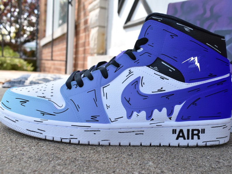 May include: White high-top sneakers with a blue and white gradient design. The sneakers have black accents and a black swoosh logo with a dripping effect. The text 'AIR' is written on the side of the shoe.