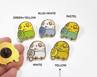 May include: Set of ten enamel pins featuring cartoon budgies in various color combinations, including green and yellow, blue and white, pastel green, white, and yellow. The pins are gold-toned and have a black pin back.