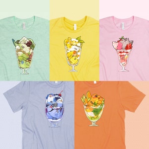 Puede incluir: Seis camisetas diferentes con periquitos coloridos y otras aves en un vaso de parfait. Cada camiseta es de un color diferente: verde, amarillo, rosa, azul, naranja y blanco.