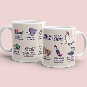 Könnte beinhalten: Zwei weiße Keramikbecher mit einem skurrilen Design. Auf einem Becher sind Illustrationen und Texte wie "Free Snacks" und "New Toys" zu sehen. Der andere Becher zeigt eine Papageien-Illustration und den Text "Birb's Guide to Household Items."
