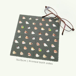 May include: A dark grey cleaning cloth, 15x15cm, with a scalloped edge, printed with colourful bird illustrations. The text "Printed both sides" is visible. Brown-framed spectacles are placed on the cloth.