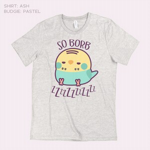 May include: A light grey t-shirt with a cartoon illustration of a yellow and blue budgie with the text "SO BORB" and "ZZZZZZZZZZ" printed on it.