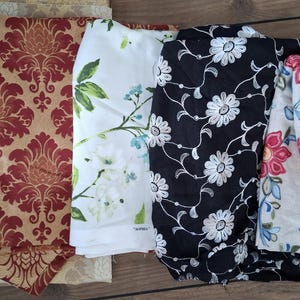 May include: Five different fabric swatches with floral patterns. The swatches are in various colors, including beige, red, white, black, and cream. The fabrics are all different textures, some are smooth and some are textured.