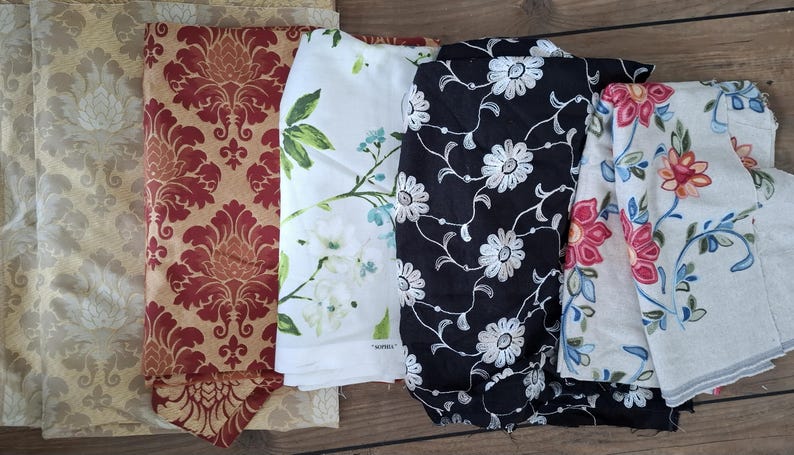May include: Five different fabric swatches with floral patterns. The swatches are in various colors, including beige, red, white, black, and cream. The fabrics are all different textures, some are smooth and some are textured.