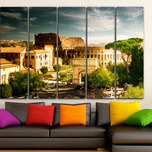 May include: A multi-panel canvas print featuring a panoramic view of the Colosseum in Rome, Italy. The image shows the ancient amphitheater, surrounded by trees and buildings, with a clear blue sky in the background.