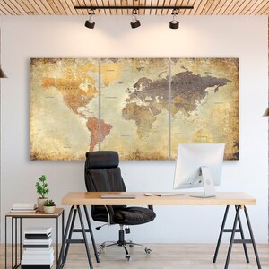 May include: A three-piece canvas print of a vintage world map in muted tones of brown, yellow, and beige. The map is displayed on a white wall in a home office setting with a black office chair, a wooden desk, and a computer monitor.