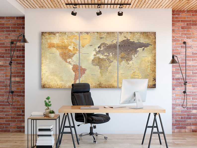 May include: A three-piece canvas print of a vintage world map in muted tones of brown, yellow, and beige. The map is displayed on a white wall in a home office setting with a black office chair, a wooden desk, and a computer monitor.