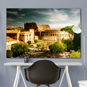 May include: A panoramic view of the Colosseum in Rome, Italy. The ancient Roman amphitheater is surrounded by trees and buildings, with a clear blue sky overhead.