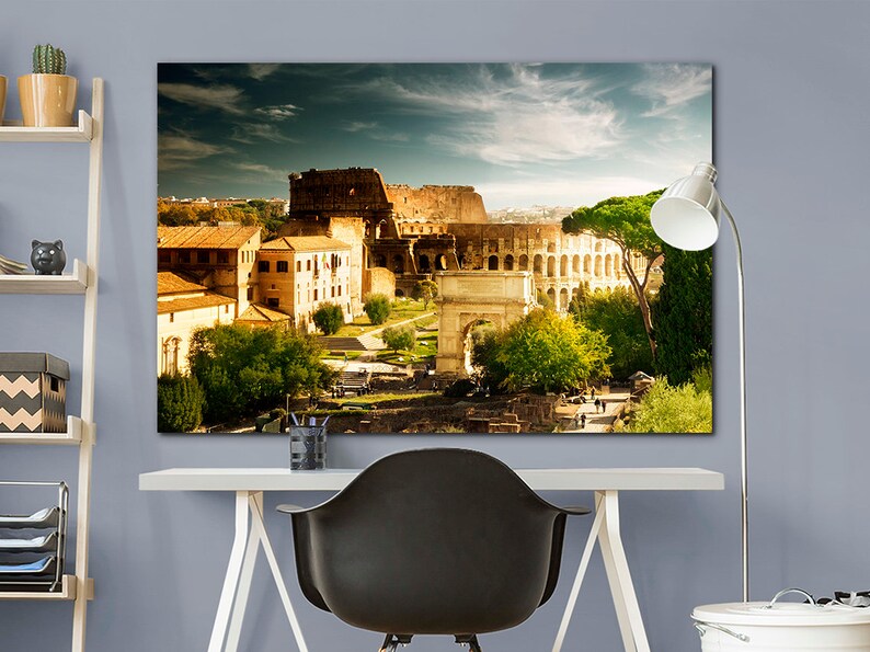 May include: A panoramic view of the Colosseum in Rome, Italy. The ancient Roman amphitheater is surrounded by trees and buildings, with a clear blue sky overhead.
