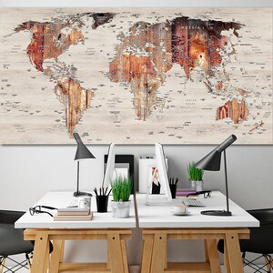 May include: A large wooden world map art piece with a light-colored background and detailed brown and orange continents. The map is mounted above a white desk with black desk lamps and office supplies.