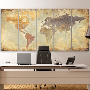 May include: A vintage-style world map print in muted tones of brown, beige, and cream. The map is divided into four panels and hangs on a white wall above a modern office desk with a black leather chair, a laptop, and a lamp.