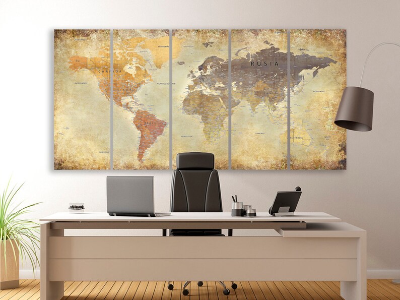 May include: A vintage-style world map print in muted tones of brown, beige, and cream. The map is divided into four panels and hangs on a white wall above a modern office desk with a black leather chair, a laptop, and a lamp.