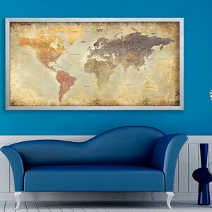 May include: A vintage-style world map in a silver frame hangs on a blue wall above a blue couch. The map has a distressed, aged look with faded colors and a textured surface. The map is surrounded by a white trim and a silver frame.