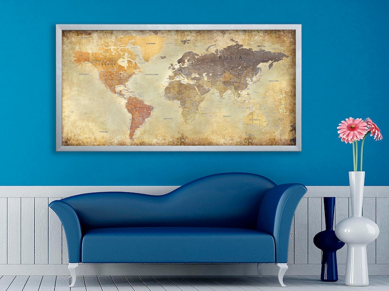 May include: A vintage-style world map in a silver frame hangs on a blue wall above a blue couch. The map has a distressed, aged look with faded colors and a textured surface. The map is surrounded by a white trim and a silver frame.