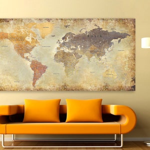 May include: A vintage-style world map print with a distressed, aged look. The map is printed on a canvas and features a light brown background with a dark brown outline of the continents. The map includes the names of countries and major cities. The map is hanging on a wall above a yellow couch.