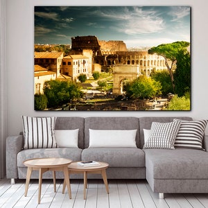 May include: A panoramic view of the Colosseum in Rome, Italy. The ancient Roman amphitheater is surrounded by trees and buildings, with a clear blue sky overhead.