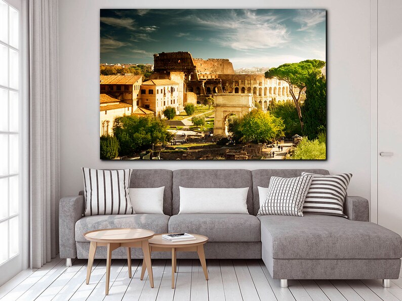 May include: A panoramic view of the Colosseum in Rome, Italy. The ancient Roman amphitheater is surrounded by trees and buildings, with a clear blue sky overhead.