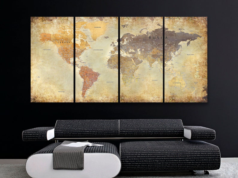 May include: A vintage-style world map print in four panels, featuring a distressed, aged look with a brown and beige color scheme. The map is divided into four sections, each showing a different part of the world. The map is displayed on a black wall above a black couch with a white ottoman.