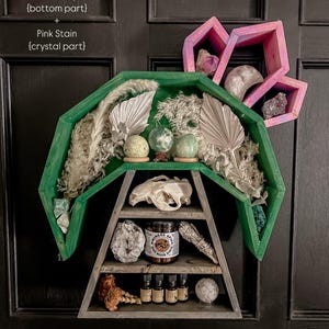 May include: A green, charcoal grey, and pink wooden shelf unit shaped like a crescent moon with a triangular shelf underneath. The shelf unit is decorated with crystals, feathers, and other decorative items. The text "no drawer & no moon phases" is written below the shelf unit.