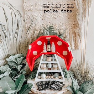 May include: A red and white mushroom-shaped shelf with polka dots, holding various items like candles, essential oils, and crystals. The text on the shelf reads "RED PAINT (top) + WHITE PAINT (bottom) w/ white polka dots".
