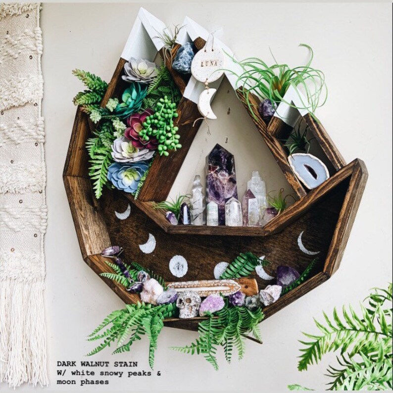 May include: A dark walnut stained wooden shelf with white snowy peaks and moon phases. The shelf is decorated with crystals, plants, and a skull. The text on the image reads "DARK WALNUT STAIN W/ white snowy peaks & moon phases".