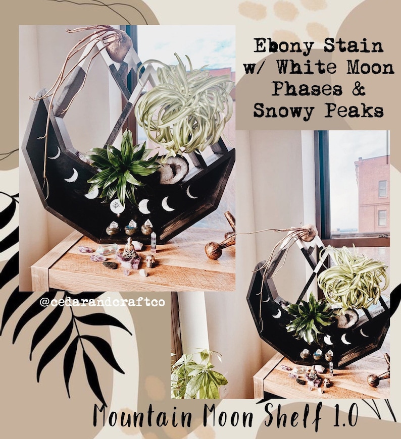 May include: Ebony-stained wooden shelf with white moon phases and snowy peaks design. The shelf holds various plants and crystals. The text on the shelf reads "Mountain Moon Shelf 1.0".