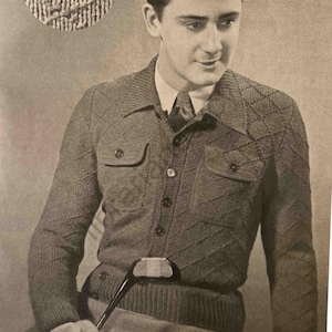 Puede incluir: Un suéter de punto marrón con un patrón de rombos y cierre de botones. El suéter tiene dos bolsillos de solapa en el pecho y un cuello. El modelo sostiene un palo de golf.