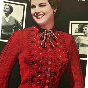 Puede incluir: Un cárdigan de punto rojo con cierre de botones y un patrón de punto decorativo. El cárdigan tiene un cuello alto y un detalle de corbata de lazo. La imagen es de una revista de punto vintage.