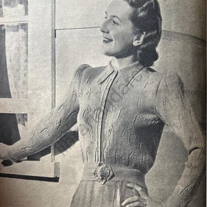 Pode incluir: Uma fotografia a preto e branco de uma mulher a usar um cardigan de malha com fecho de botões e um broche decorativo. O cardigan tem um padrão texturizado e uma gola. A mulher está a sorrir e tem a mão na anca. O texto "LINCOLN Model No. L1010" é visível na parte inferior da imagem.