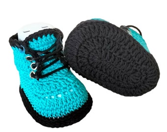 May include: A pair of crocheted baby booties in teal blue and black. The booties have a lace-up design and a black crocheted sole.