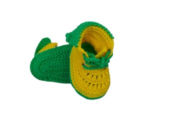 May include: A pair of crocheted baby booties in green and yellow. The booties have a lace-up design and are made with a soft yarn.