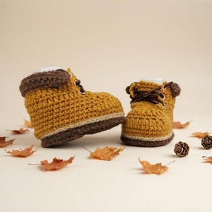 May include: A pair of mustard yellow crochet boots with dark brown cuffs and dark brown laces. The boots feature a thick, textured stitch pattern and a dark brown sole. The design mimics the appearance of a classic work boot style.