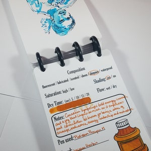 May include: A close-up of a handwritten ink swatch card with notes about the ink's properties. The ink is a vibrant orange color with a shimmer finish. The card includes the brand name "Jacques Herbin" and the ink name "Cornaline d'Egypte".