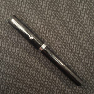 May include: A black fountain pen with silver accents. The pen has a shiny, smooth finish and a silver clip. The pen's design is simple and elegant, suitable for writing or calligraphy. The pen is set against a dark patterned background.
