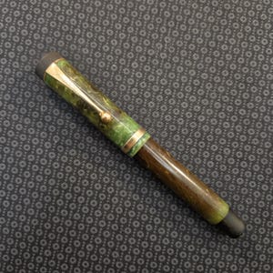 May include: A vintage fountain pen with a green and brown marbled barrel and a gold-colored clip. The pen has a black nib and a black end cap. The pen is a classic writing instrument.