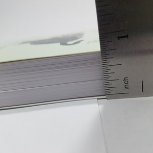 May include: Close-up of the edge of a book with a ruler measuring the thickness of the book. The ruler is marked in inches and shows a measurement of 1 inch.