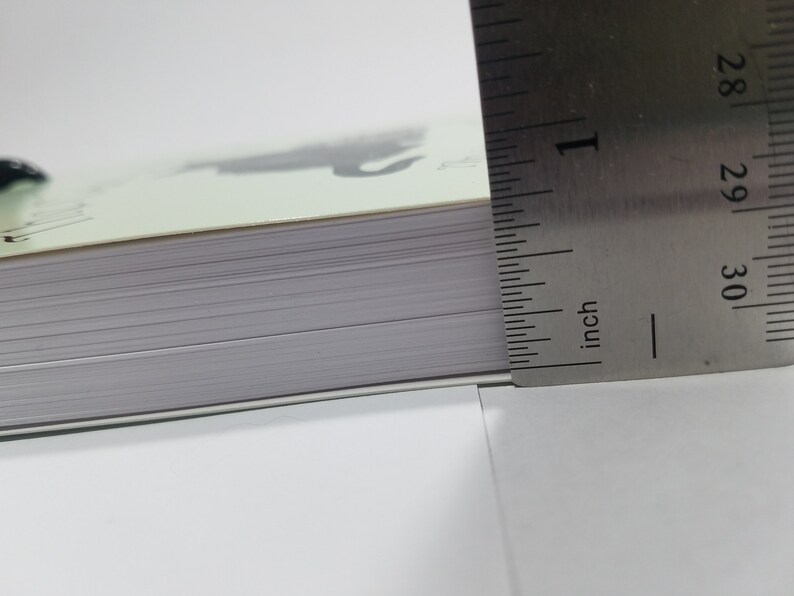 May include: Close-up of the edge of a book with a ruler measuring the thickness of the book. The ruler is marked in inches and shows a measurement of 1 inch.