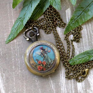 May include: Antique brass pocket watch with a detailed fairy illustration on the face. The watch features a chain and a decorative winding stem. The fairy is depicted with wings, roses, and a crescent moon background.