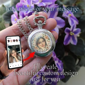 Peut inclure: Un pendentif de montre de poche argenté avec une chaîne, présentant une photo personnalisée entourée d'éléments floraux. L'image montre également un smartphone affichant une photo similaire. Le texte sur l'image dit : "Your photo or your message" et "I'll create beautiful custom design just for you."