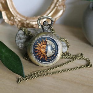 Peut inclure: Montre de poche de style antique avec une finition bronze et une chaîne. Le cadran de la montre présente un motif céleste, avec un soleil et une lune divisés en deux, sur fond bleu étoilé. Un accessoire vintage.