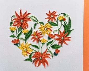 Könnte beinhalten: Ein handgefertigtes Papier-Quilling-Kunstwerk mit einem herzförmigen Blumendesign. Das Kunstwerk zeigt orange, gelbe und grüne Blumen mit filigranen Details. Der Hintergrund ist weiß, mit einem orangefarbenen Rand.