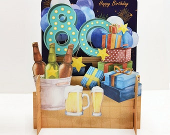 Puede incluir: Una tarjeta de cumpleaños 3D pop-up con un 80 azul y verde rodeado de globos, regalos y un cubo de cerveza. La tarjeta dice "Feliz cumpleaños".
