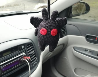 May include: Black crocheted plush toy with red eyes hanging from the rearview mirror of a car.