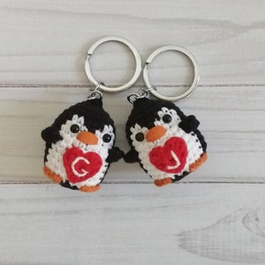 May include: Two crocheted penguin keychains with black and white bodies and red hearts with the letters "G" and "J" on them.